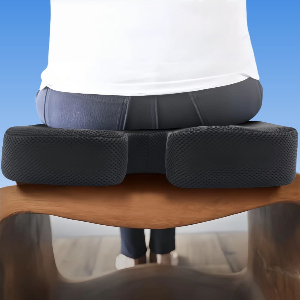 Person sitting on a black ergonomic seat cushion on a wooden chair with a blue background