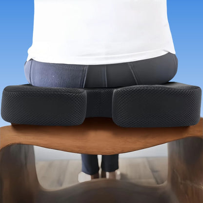 Person sitting on a black ergonomic seat cushion on a wooden chair with a blue background