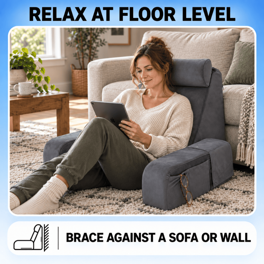 A woman sits on a dark gray floor-level reclining chair in a living room, holding a tablet. The chair is positioned in front of a sofa and wall, with text overlays reading 'RELAX AT FLOOR LEVEL' and 'BRACE AGAINST A SOFA OR WALL'.