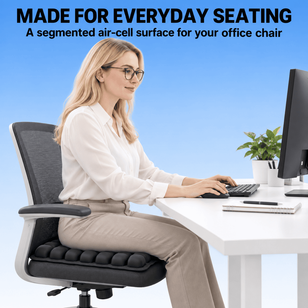 A woman wearing glasses sits in a modern office chair at a white desk, using a computer. The chair has a black segmented air-cell seat cushion and a gray mesh backrest.